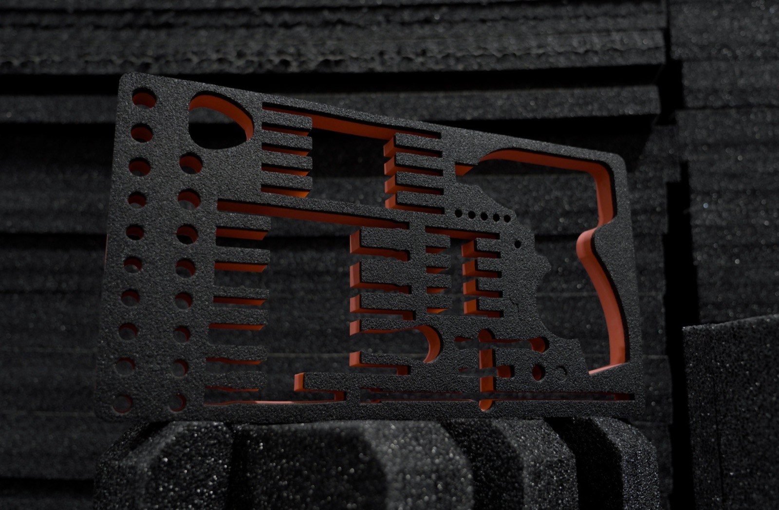 Intricately cut black foam insert with orange backing, held against stacked foam